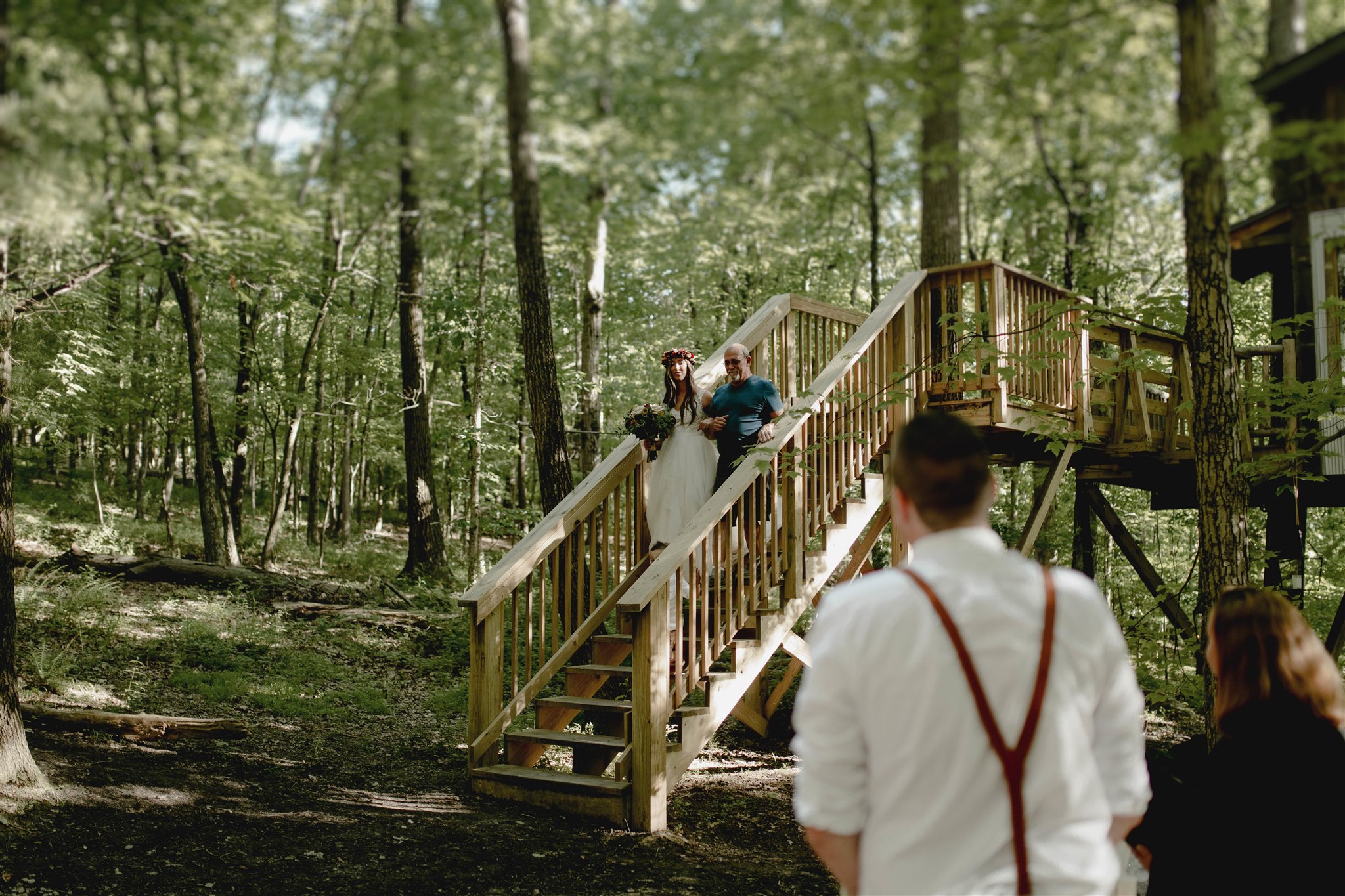 a bride and groom walking down a wooden staircase in the woods