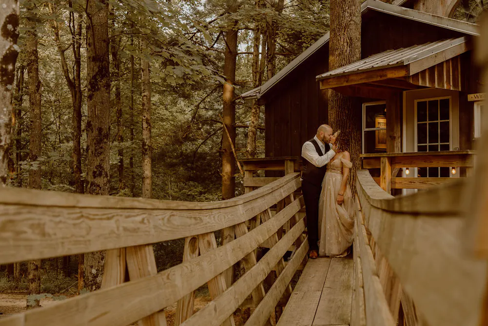 a man and woman standing on a bridge in the woods