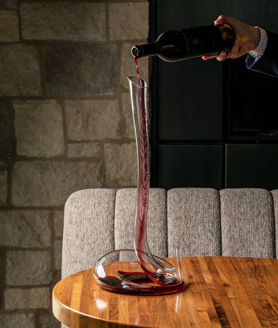 bottle of red wine being poured into a long spiral decanter