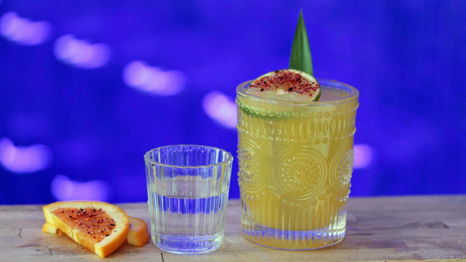 a glass of Margarita, small glass of mezcal and orange slices