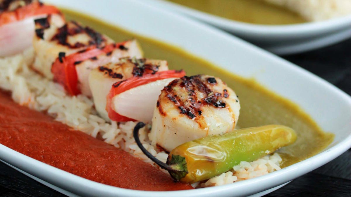 a bowl of grilled scallops, veggies, sauce and rice on a plate