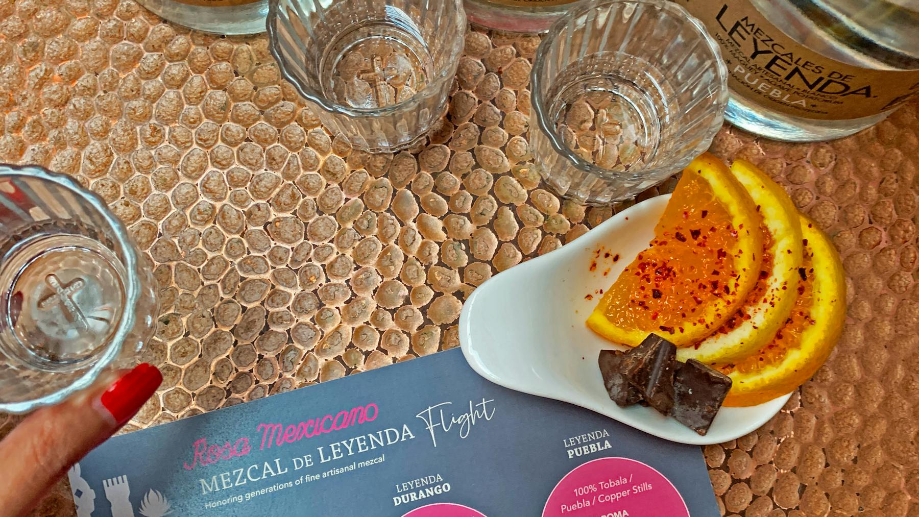 Mezcal flight in hand with orange slices and chocolate