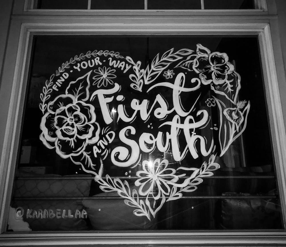 a black sign with white text hanging from a window