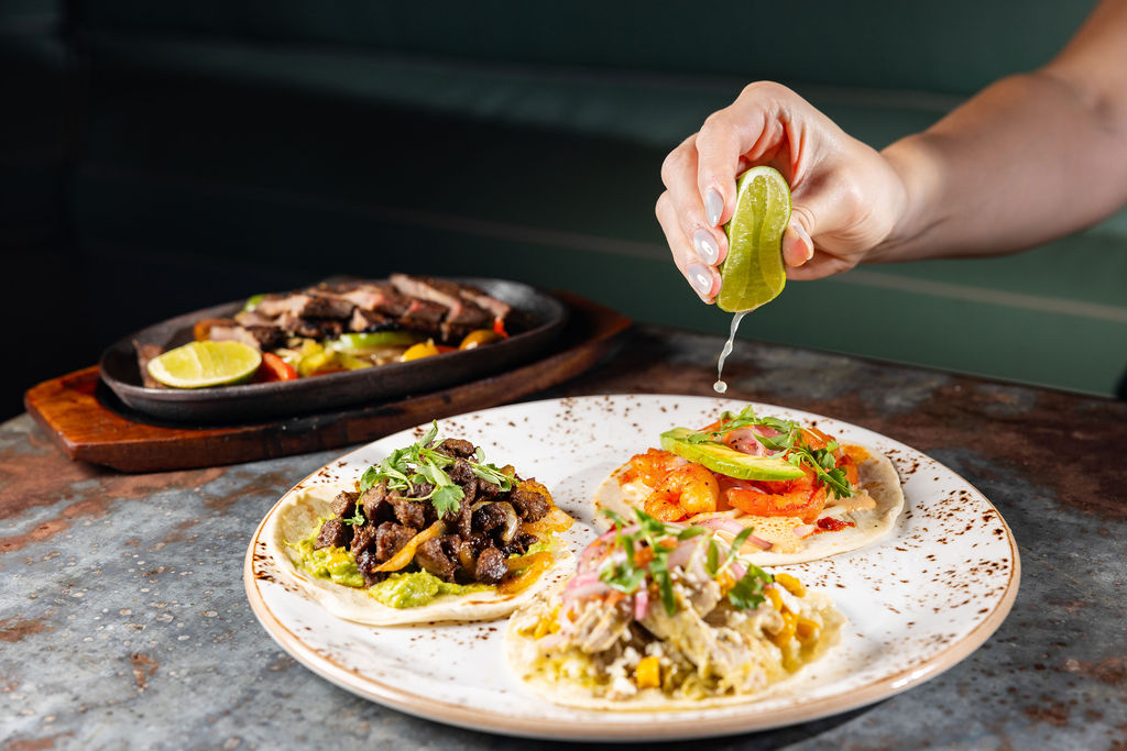 a person squeezing lime on a plate of tacos