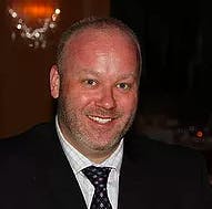 a man wearing a suit and tie smiling at the camera