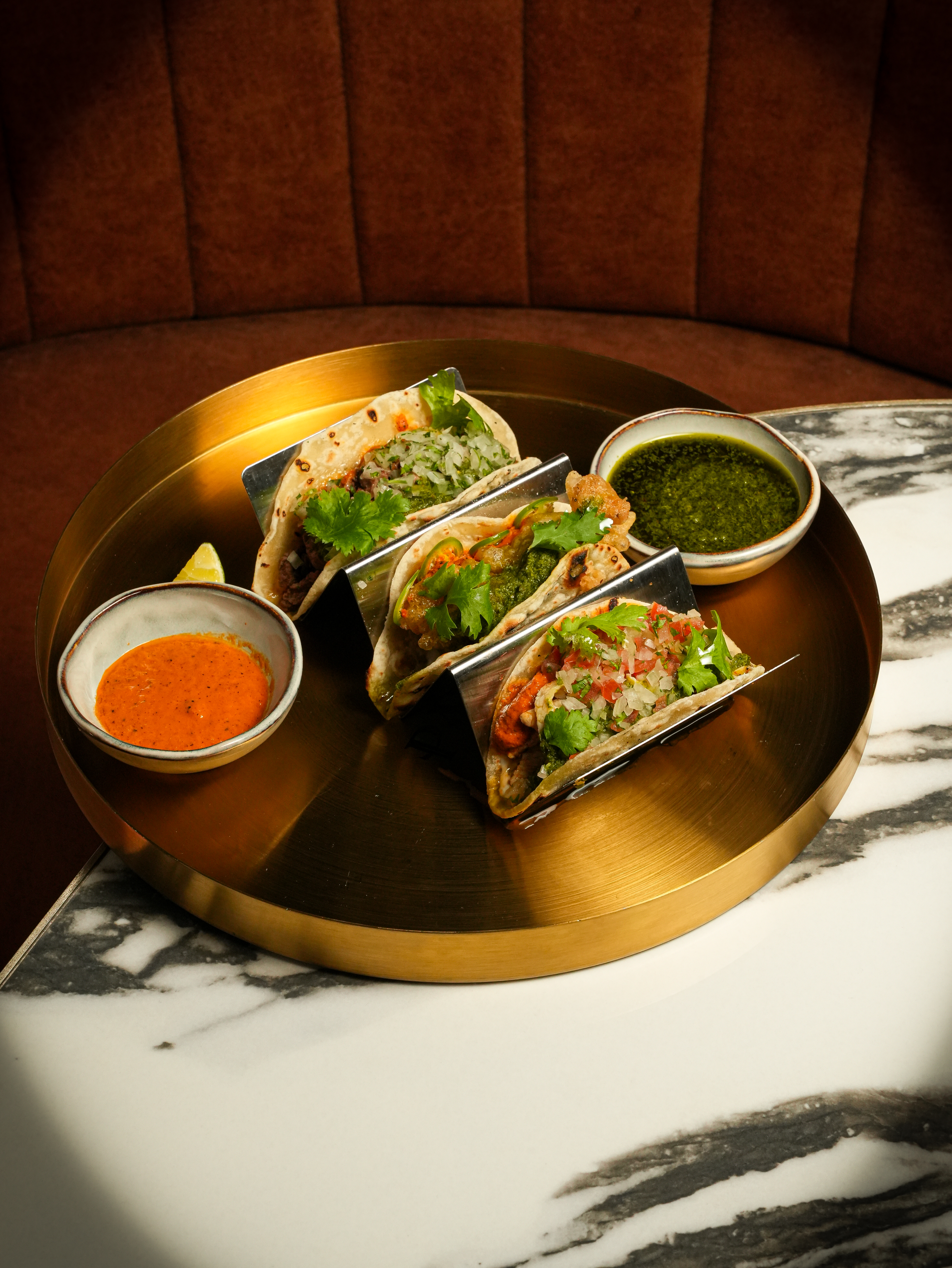 a plate of tacos with sauces on a marble table