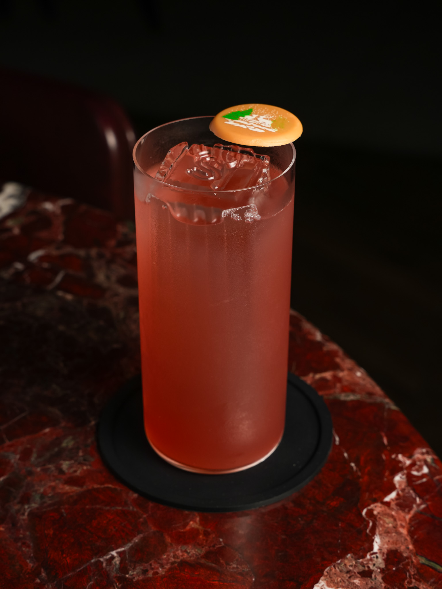 a glass of pink liquid with a small orange button on top
