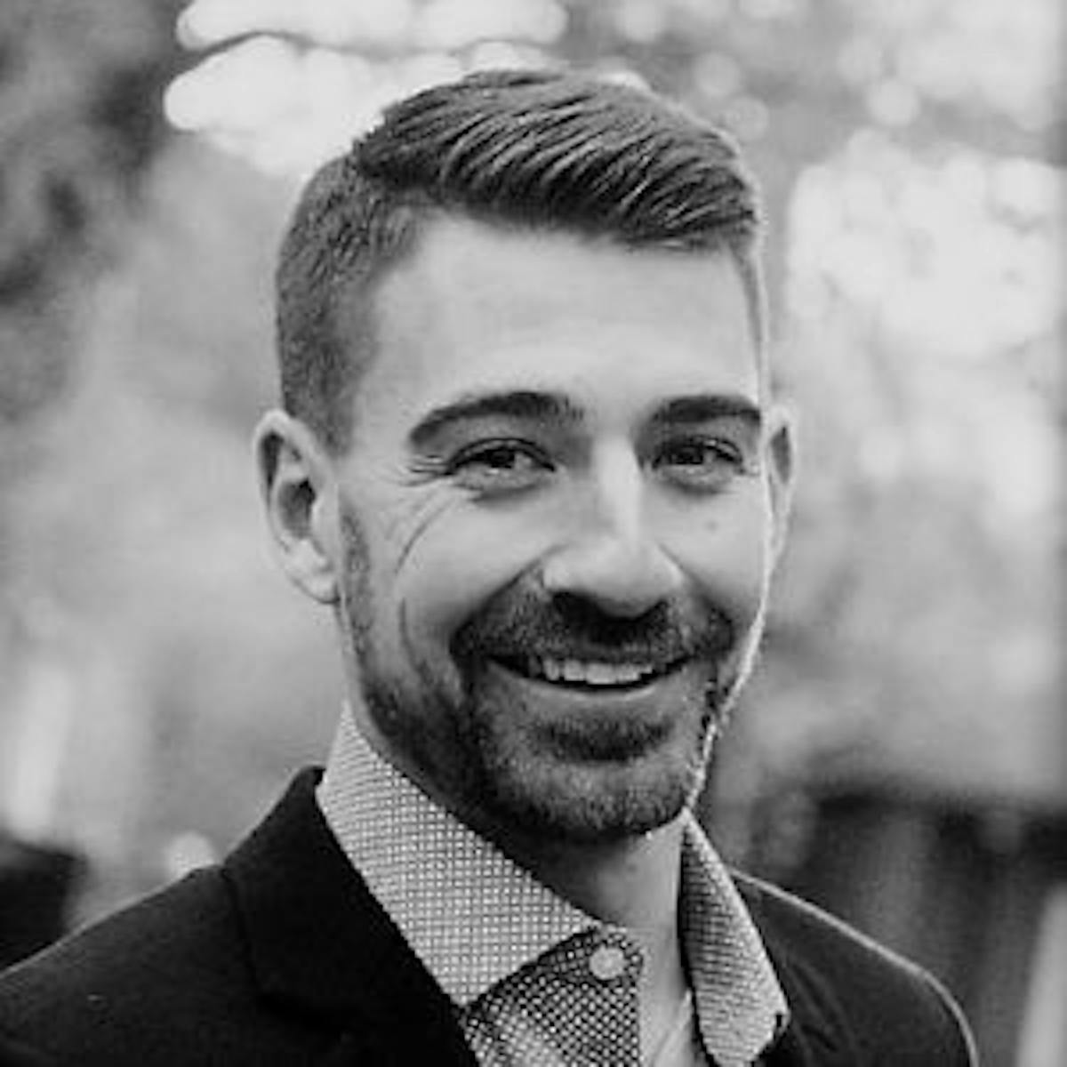 a man wearing a suit and tie smiling at the camera