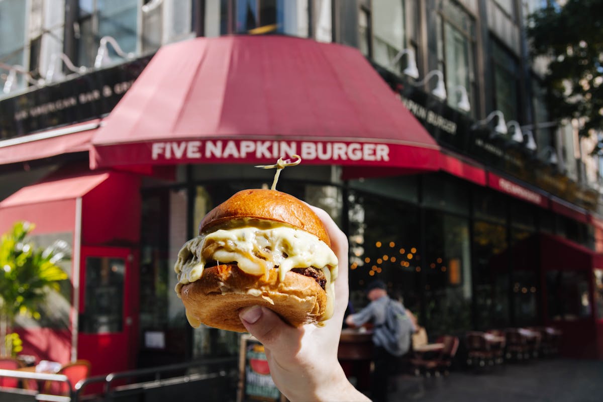 a person holding a burger in front of the restaurant