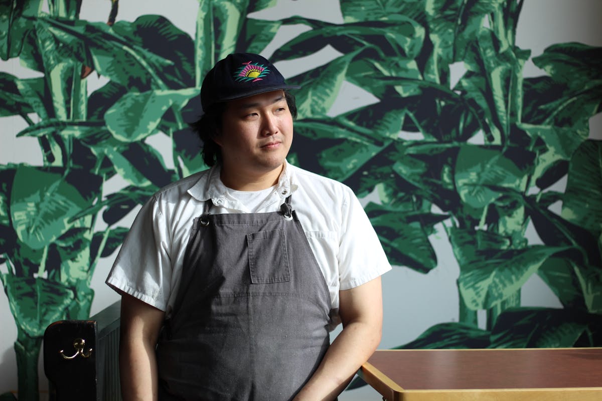 Chef Ray Hui standing in the West Asheville restaurant location. Leaf wall paper in the background.