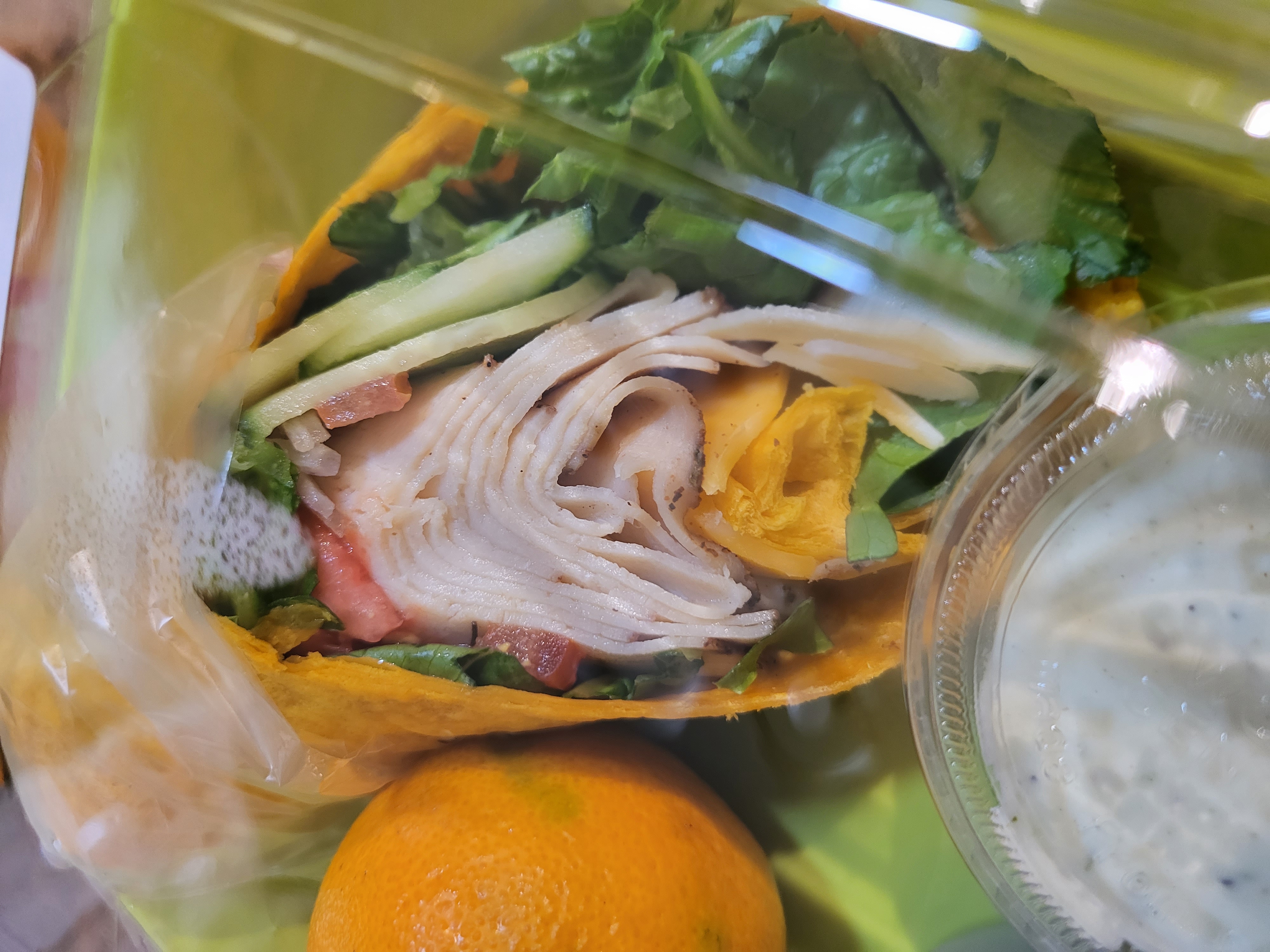 a close up ofa plastic container of Roasted Deli Turkey & Cheese on a Jalapeno Queso Wrap
