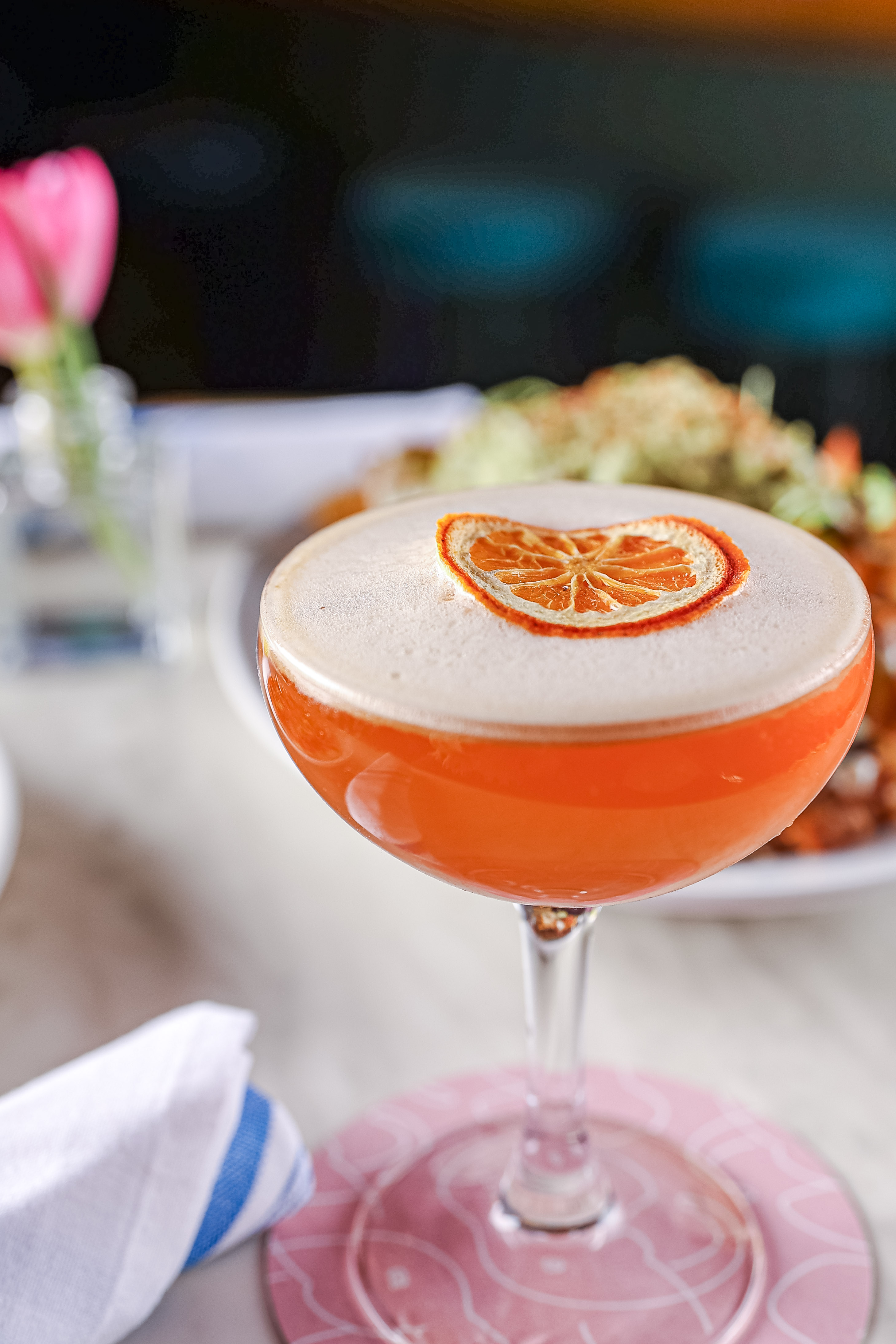 The Sunset Sour Cocktail served in a coupe glass with a freeze dried orange