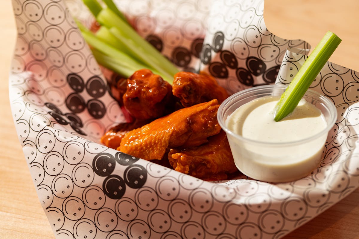 Basket of wings served with celery sticks and a sauce cup