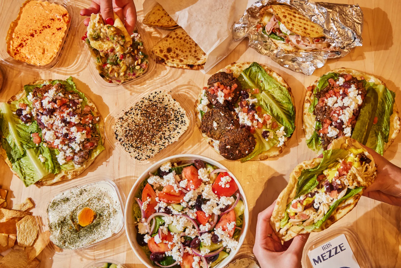 Mediterranean spreads, pita sandwiches, falafel, and Greek salad shared across a table for lunch in Boston.