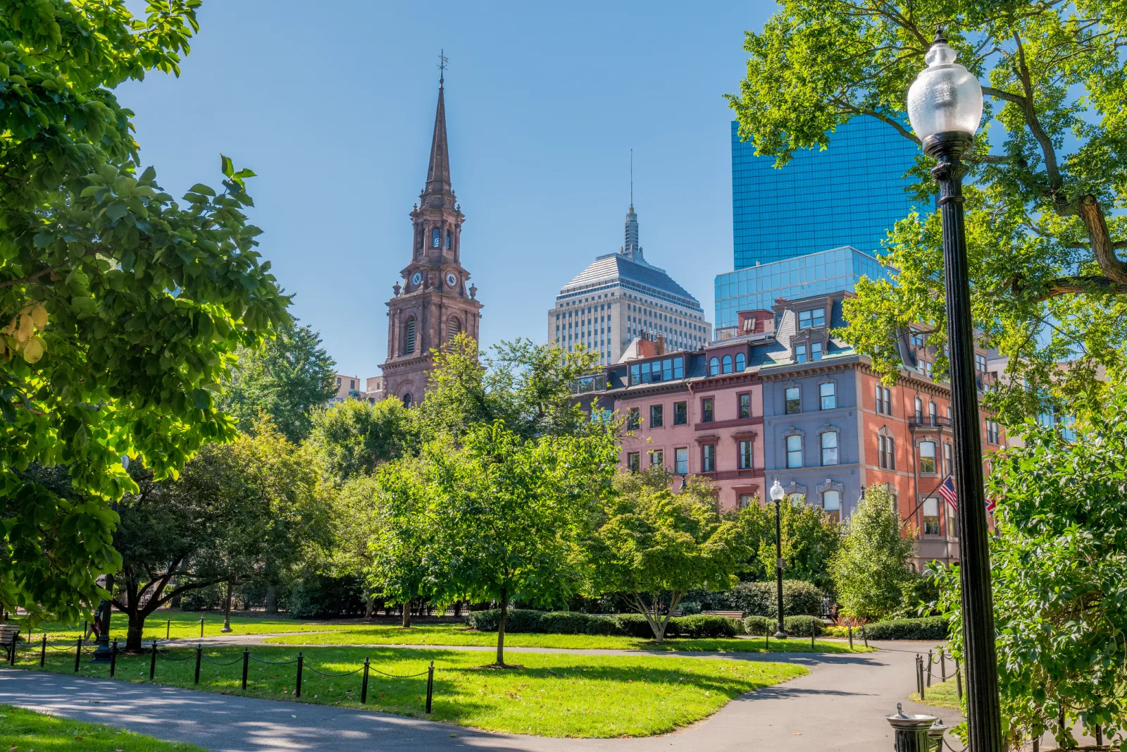 Boston Common with historic church steeple, green park, and downtown skyline view of Boston Financial District.