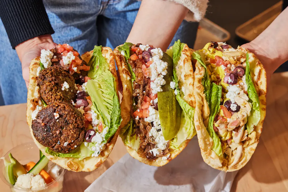 Three stuffed pita sandwiches with falafel, chicken, and beef topped with lettuce, feta, and olives for lunch in Boston.