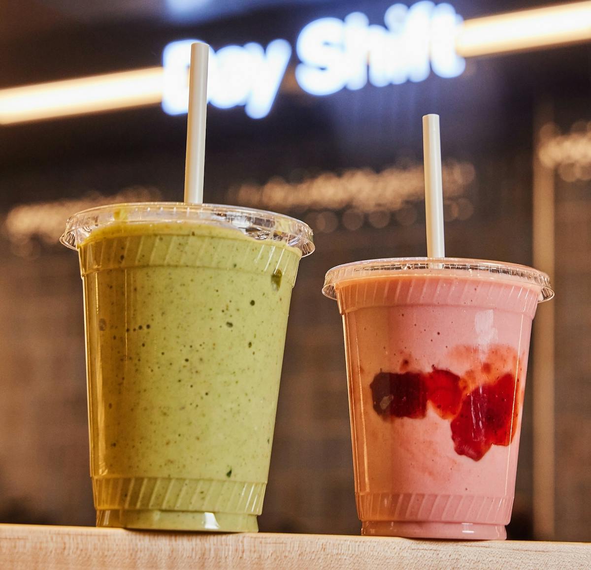 A green smoothie and strawberry smoothie on a table