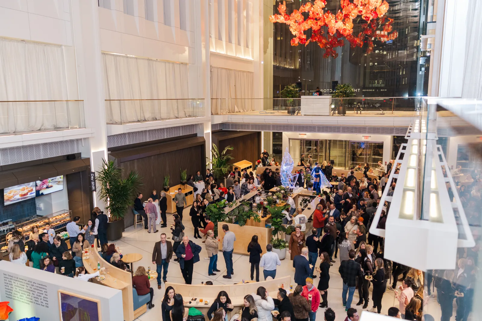 Large gathering in a modern atrium with guests mingling around a central bar, a great example of corporate event planning.