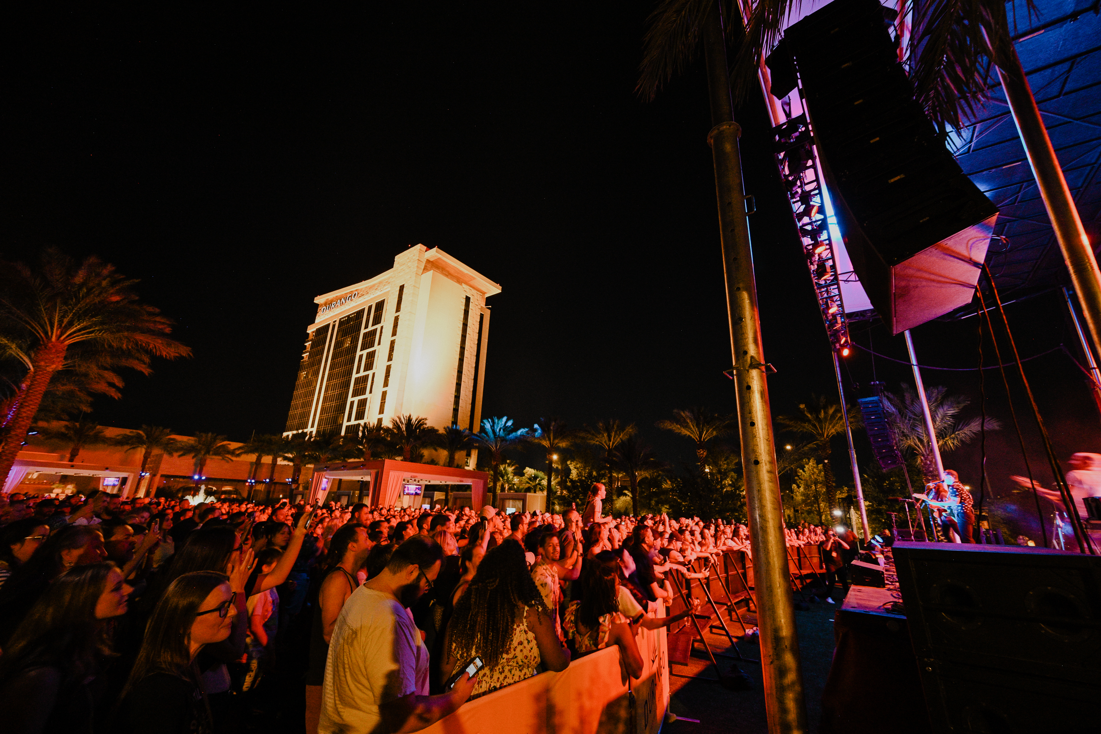 Guests watching a live concert at Bel-Aire Backyard with Durango Resort illuminated behind the outdoor stage in Las Vegas.