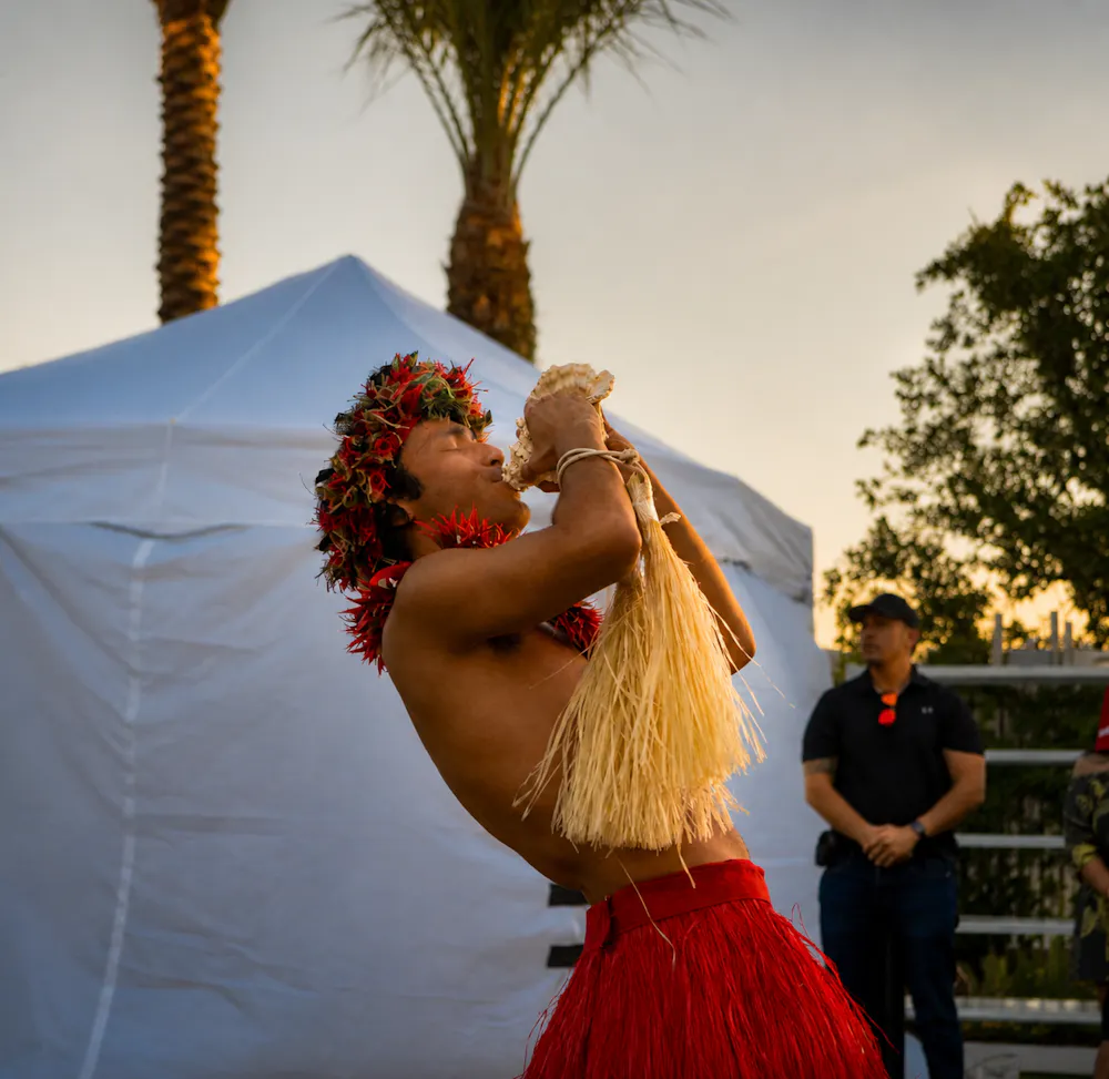 Polynesian performer blowing a conch shell during Aloha Fridays at Bel-Aire Backyard resort pool, celebrating Hawaiian culture and island-inspired entertainment.