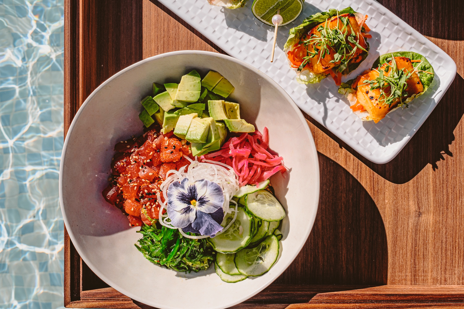 Fresh ahi poke bowl and salmon lettuce wraps served poolside at Bel-Aire Backyard, featuring vibrant flavors and elevated outdoor dining in Las Vegas at a luxury resort pool.