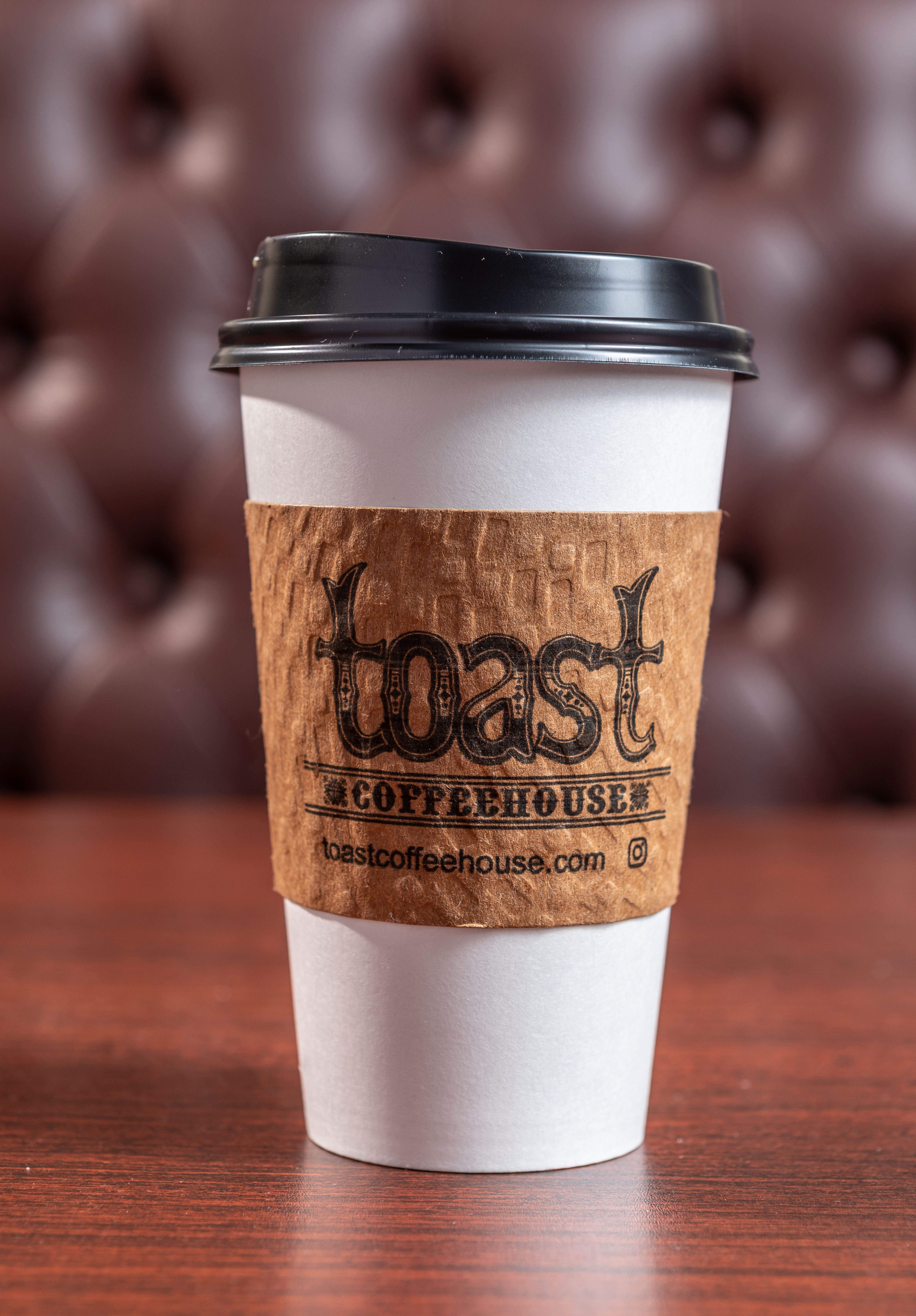 a paper coffee cup with sleeve of Toast Coffeehouse logo