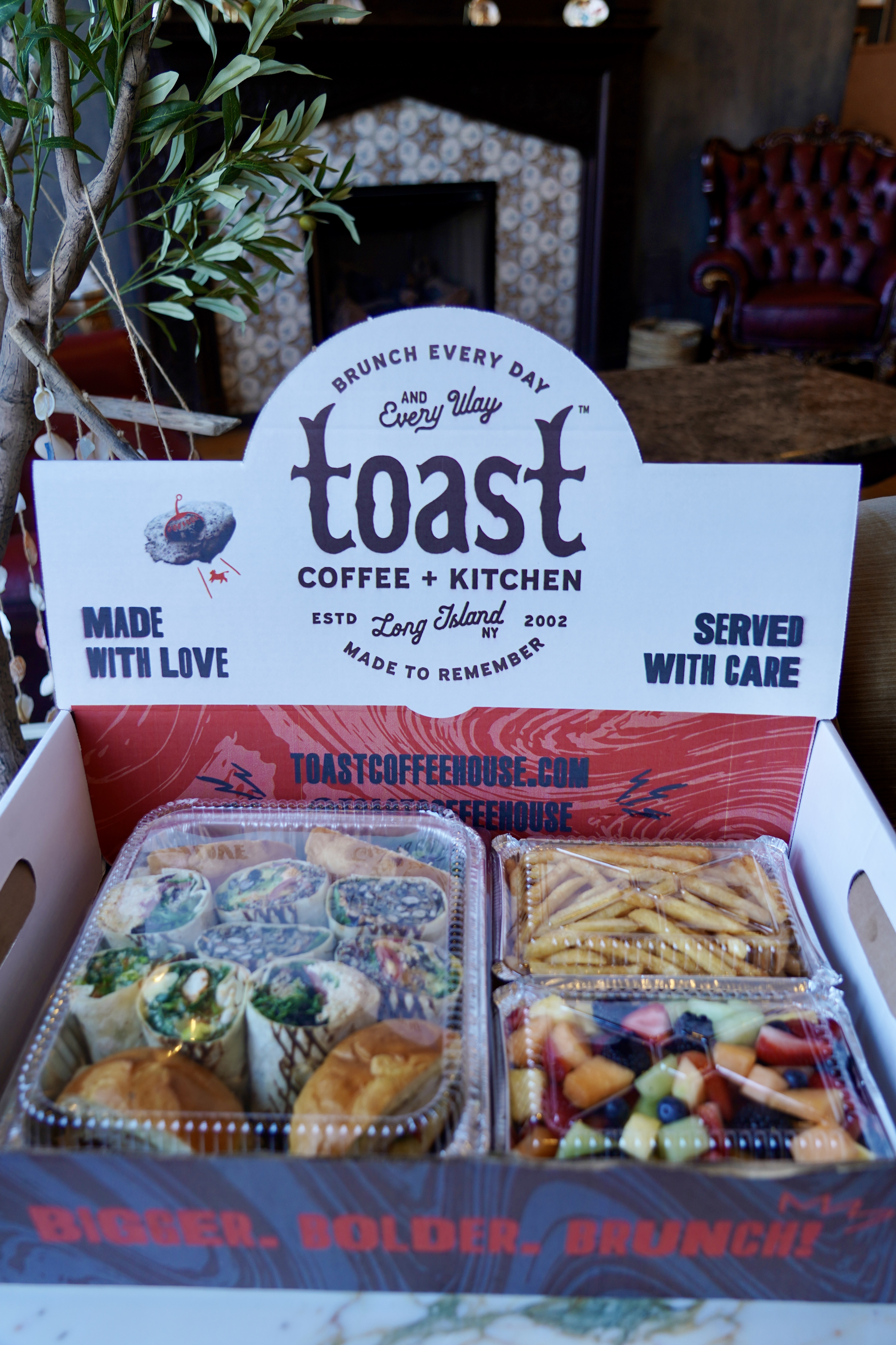 A box of food with assorted lunch wraps and sandwiches, french fries and fresh mixed fruit