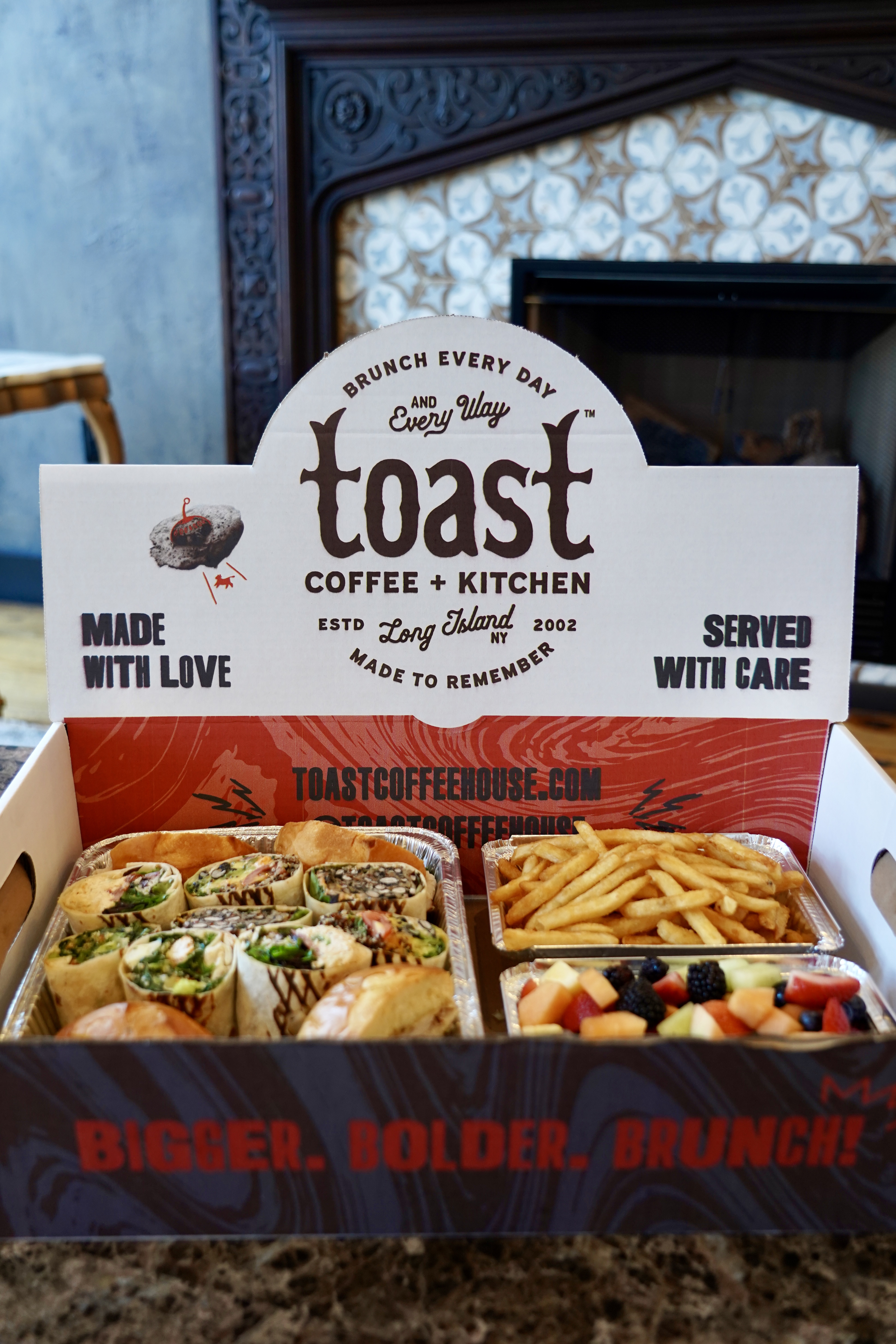 A box of food with assorted lunch wraps and sandwiches, french fries and fresh mixed fruit