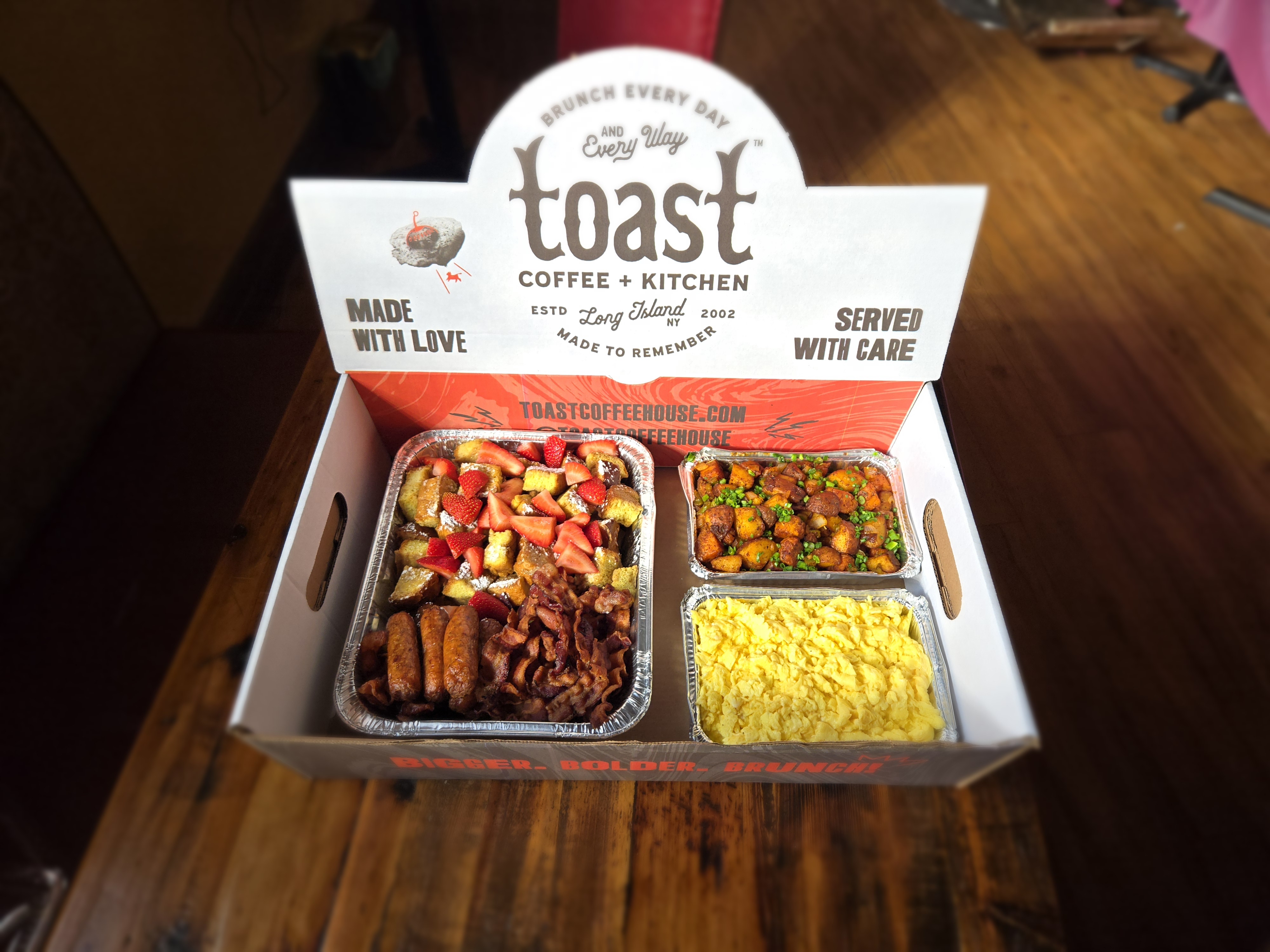 A box of french toast, bacon, sausage, scrambled eggs and home fries