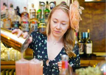 A woman with a facinator pouring a cocktail