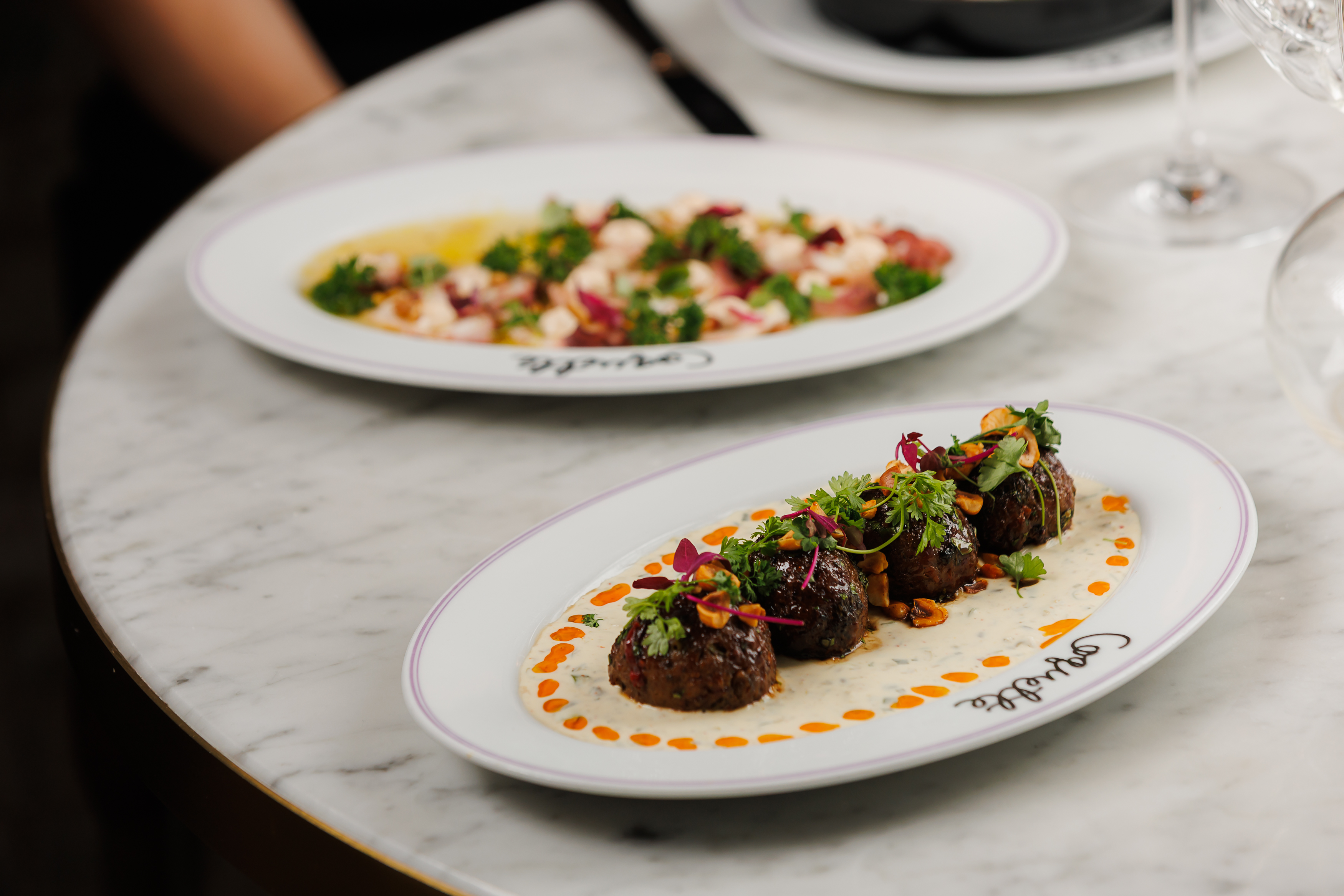 Lamb Meatballs caper crème fraîche, orange-date glaze, crushed hazelnuts, harissa chili oil