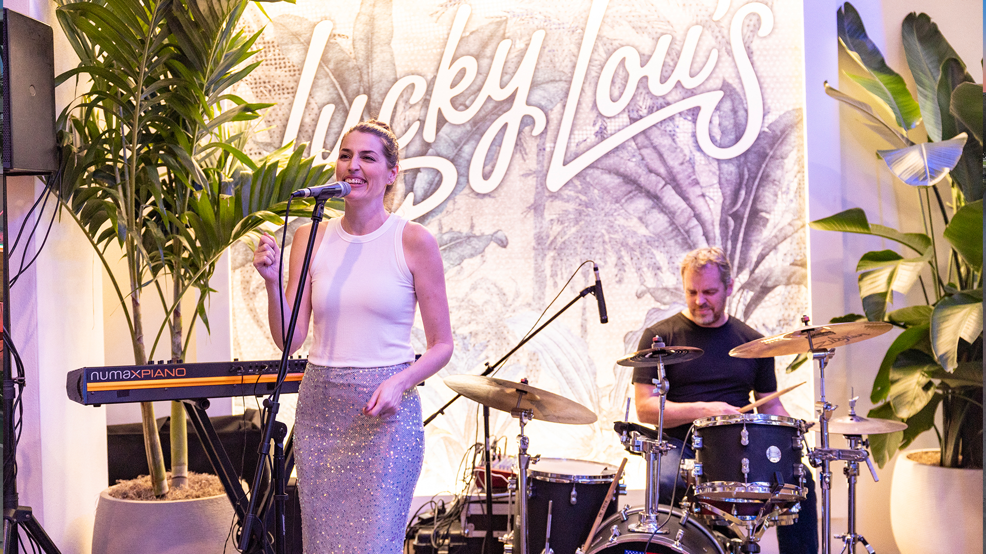 a woman singing into a microphone with a man playing drums