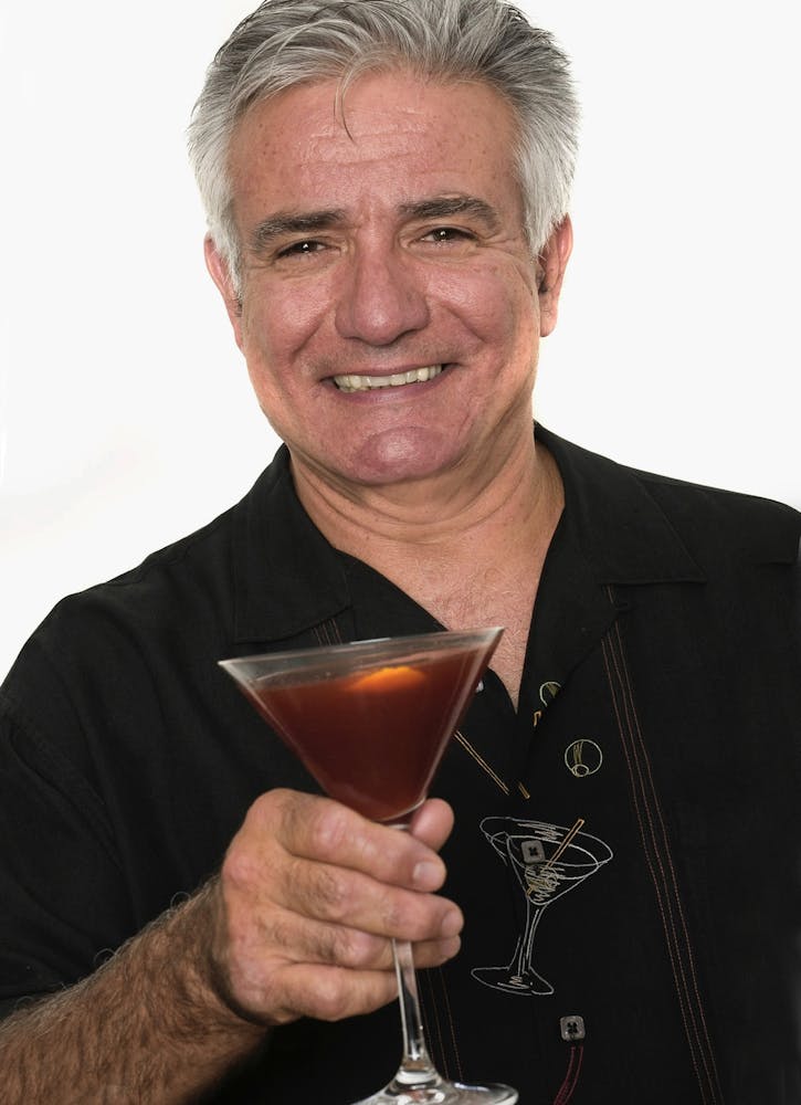 Dale DeGroff holding a wine glass posing for the camera