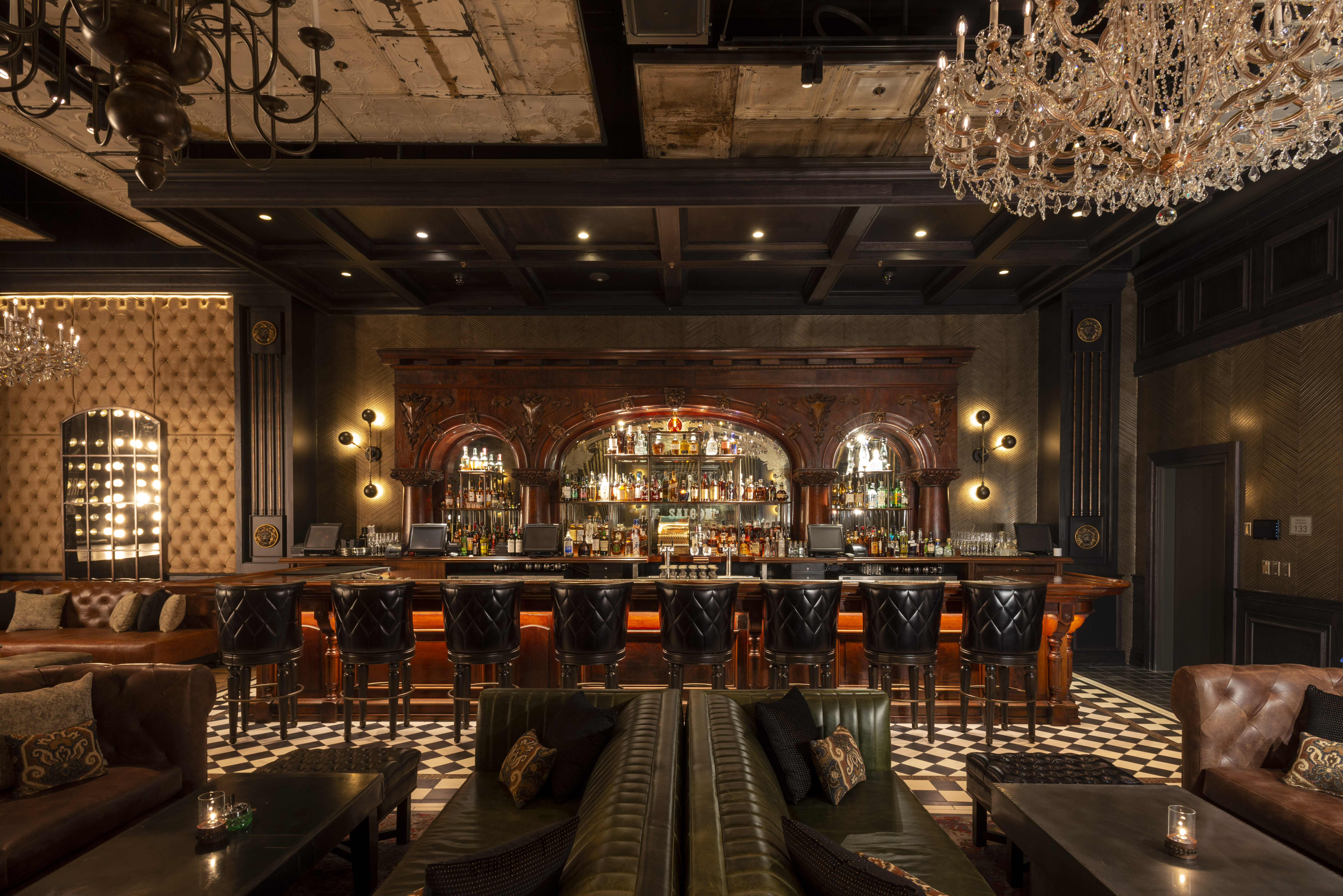 Dimly lit bar inside The Barbershop, a hidden Las Vegas speakeasy, with an ornate carved-wood back bar and crystal chandelier
