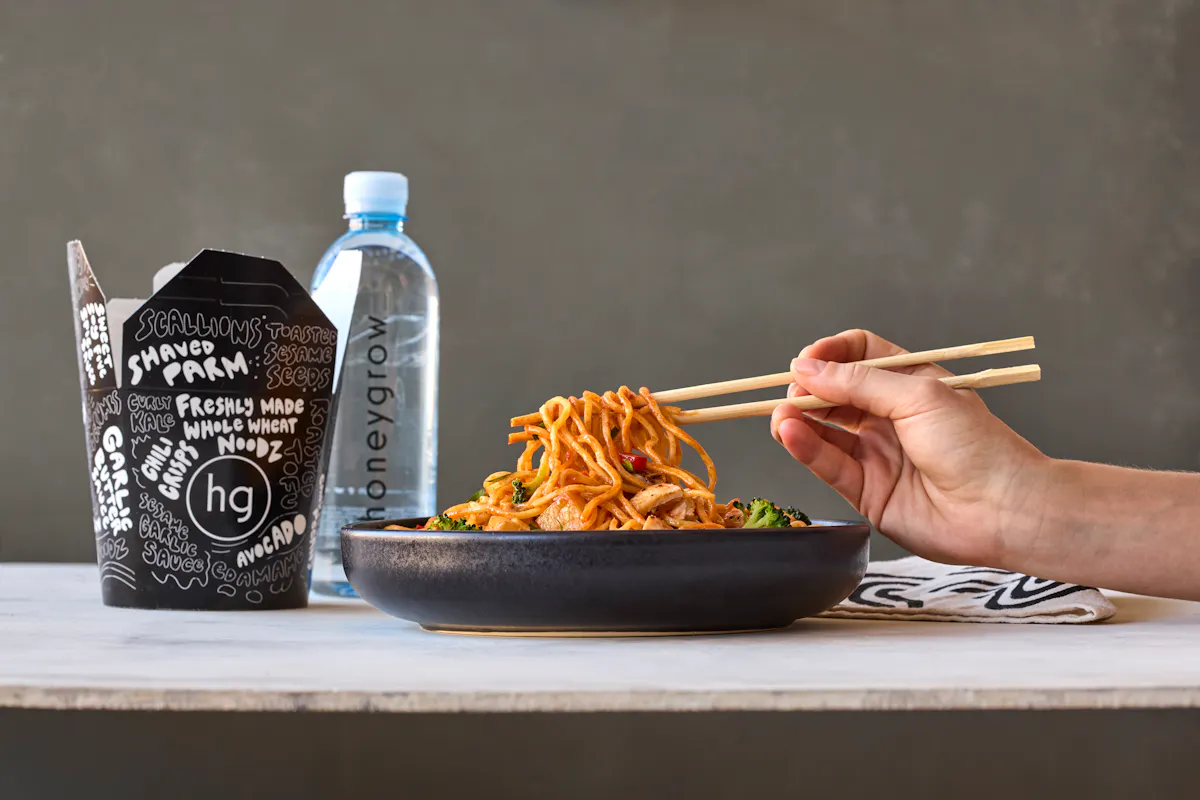 a tray of food on a table with chopsticks pulling up noodles