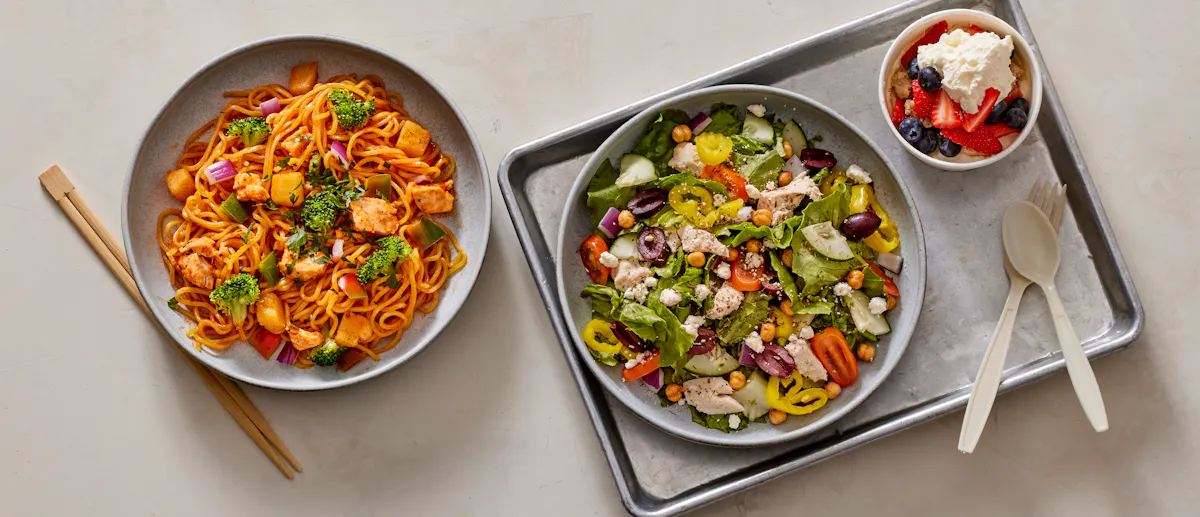 a bowl of stir-fry, salad and a honeybar fruit dish on a table