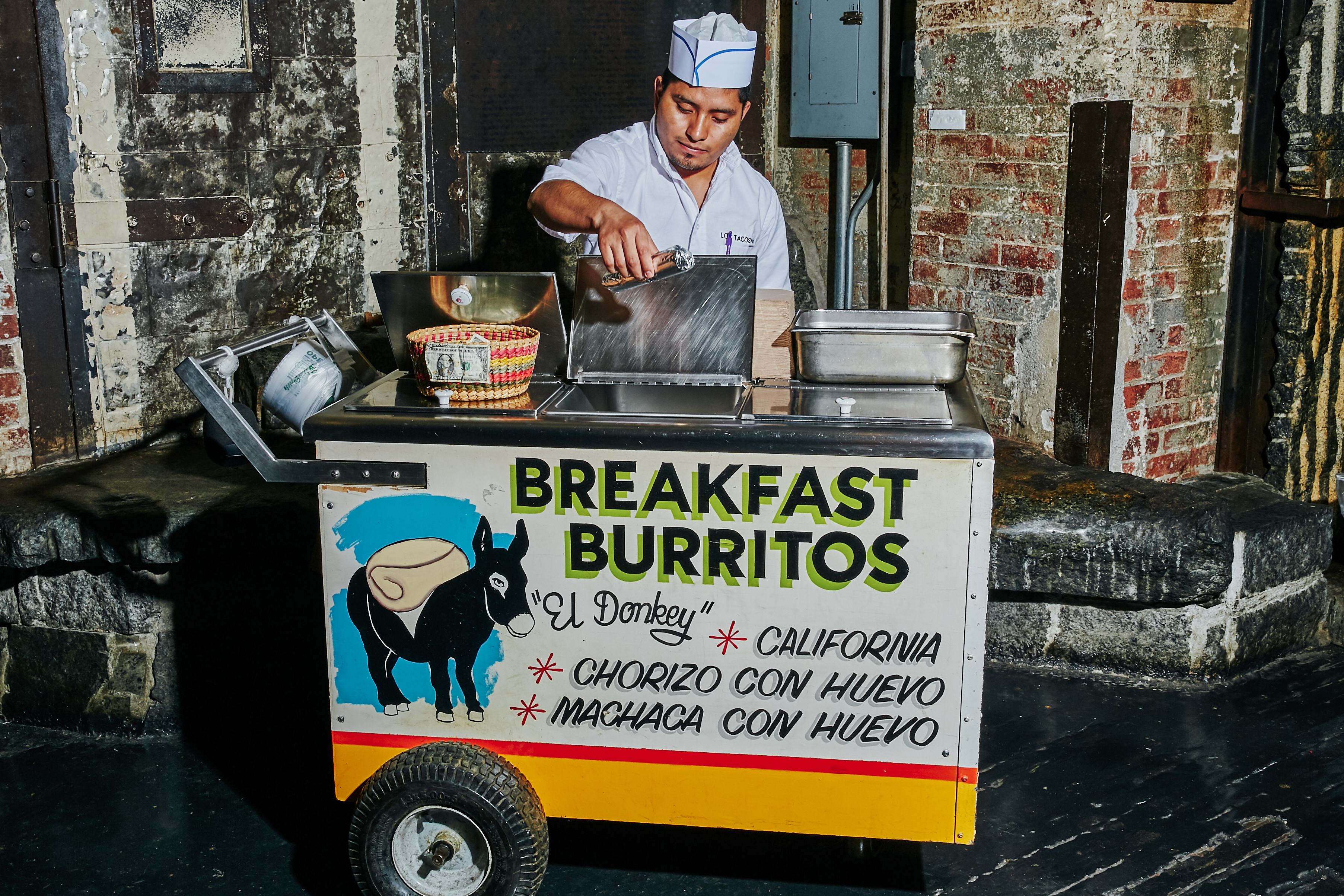 A Los Tacos No.1 employee standing behind a burrito cart.