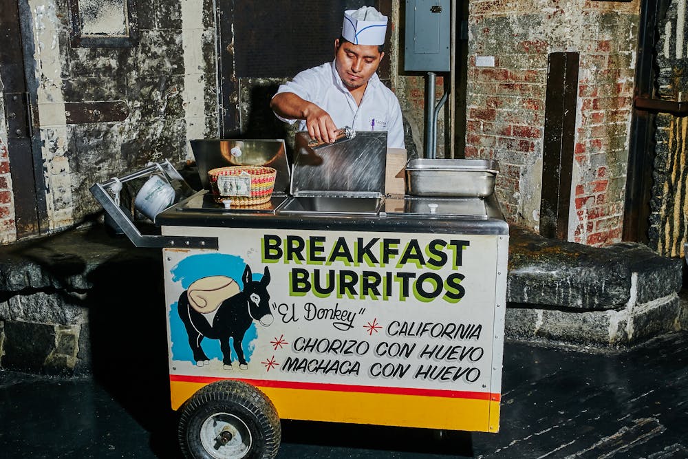 A Los Tacos No.1 employee standing behind a burrito cart.