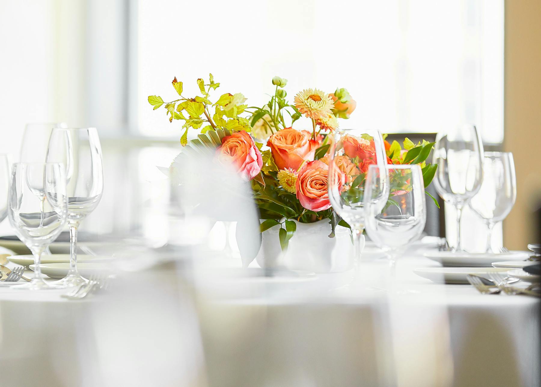 a vase of flowers on a table with wine glasses