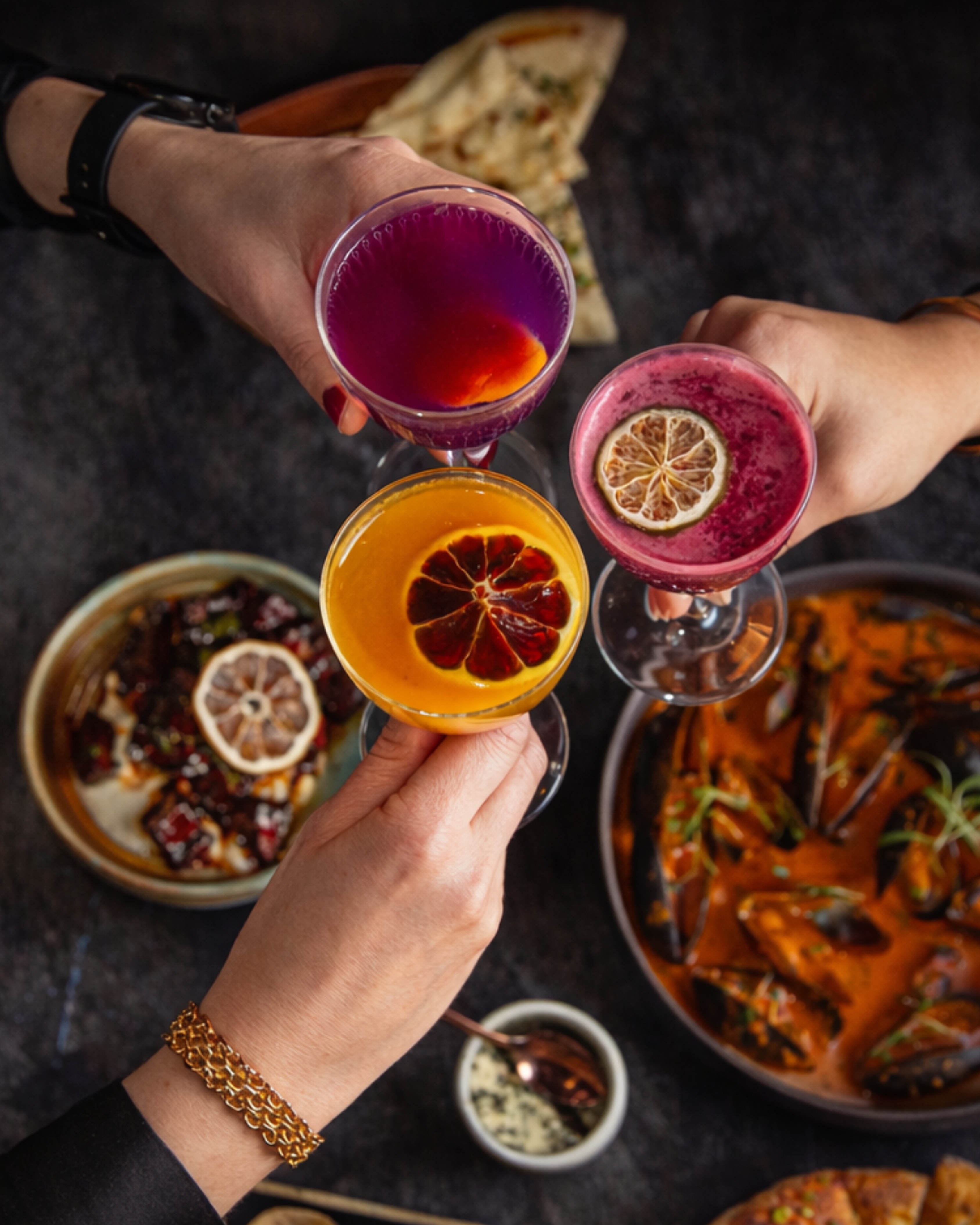 a group of hands holding glasses with different colored drinks