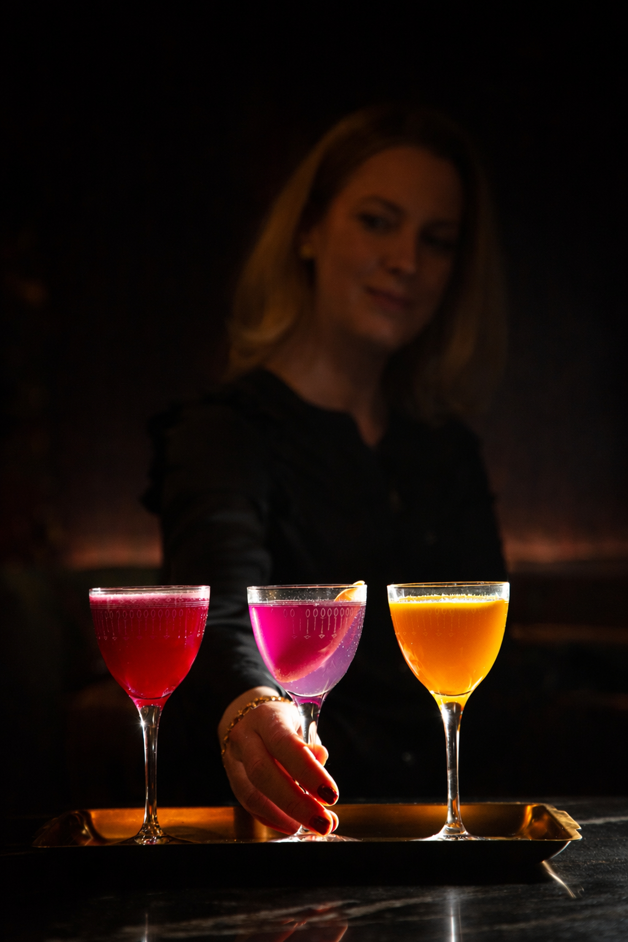 a woman holding a glass of colorful drinks