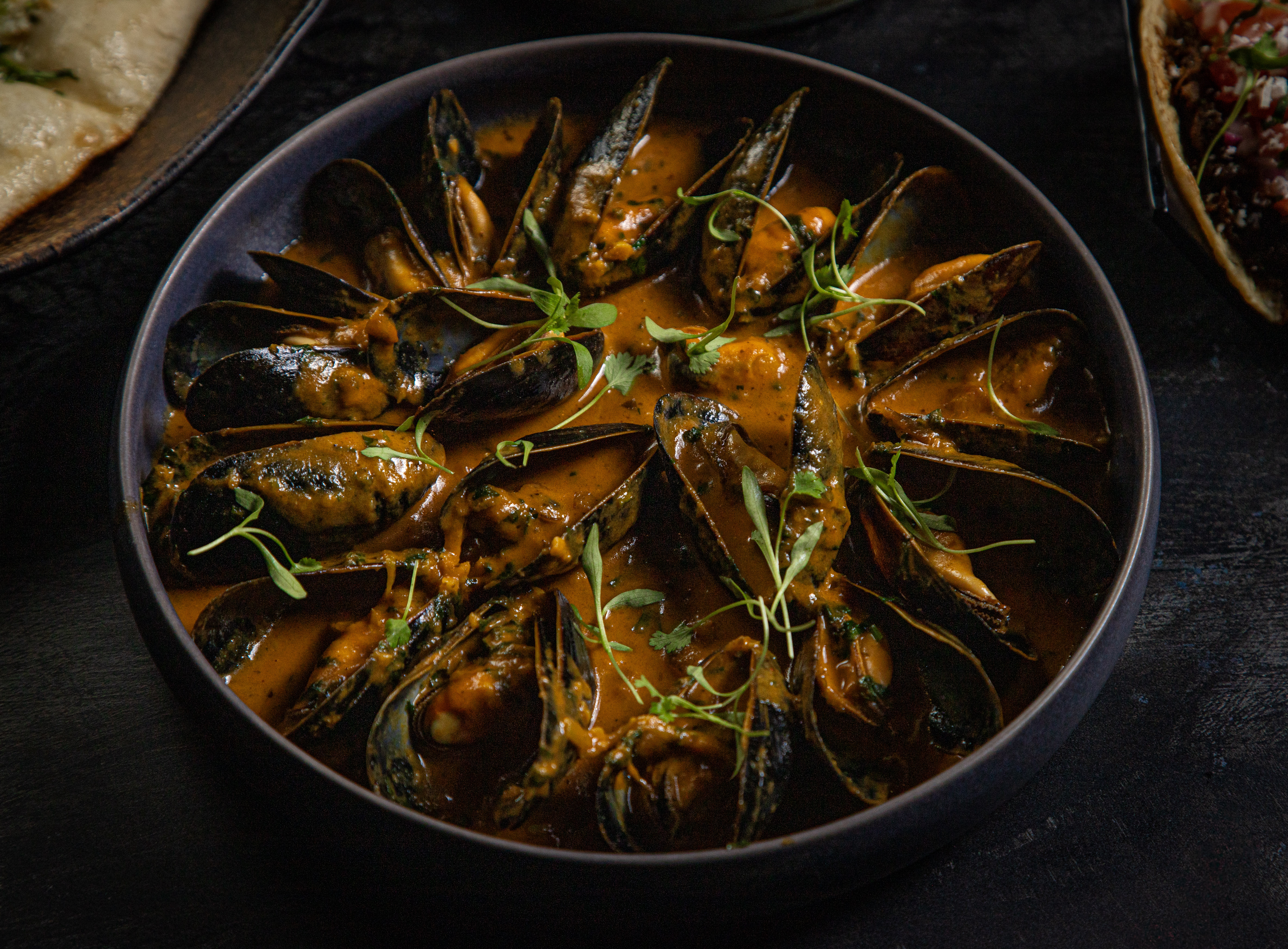 a bowl of mussels with sauce and herbs