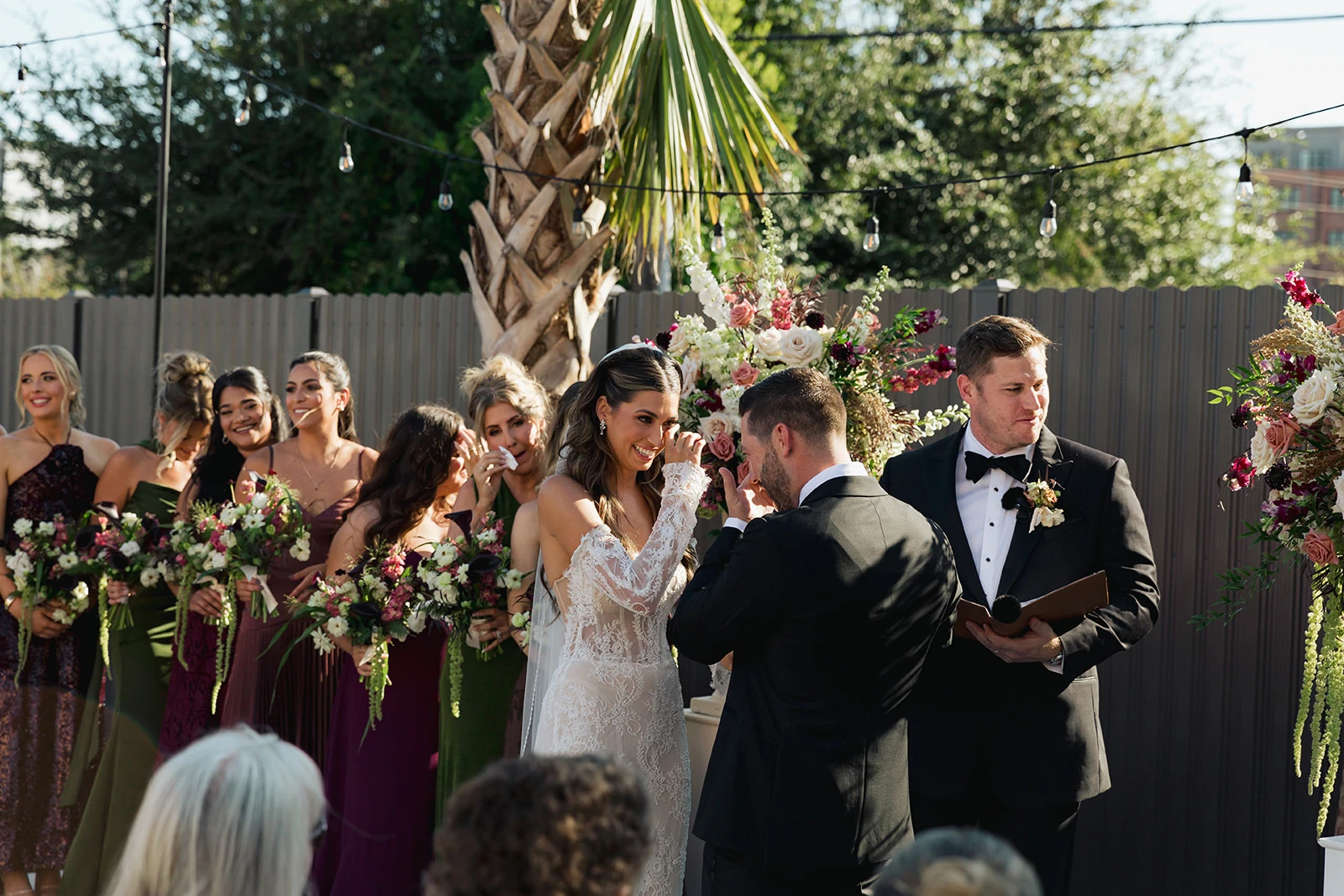 A couple exchanging vows surrounded by their wedding party and garden flowers at The Waverly