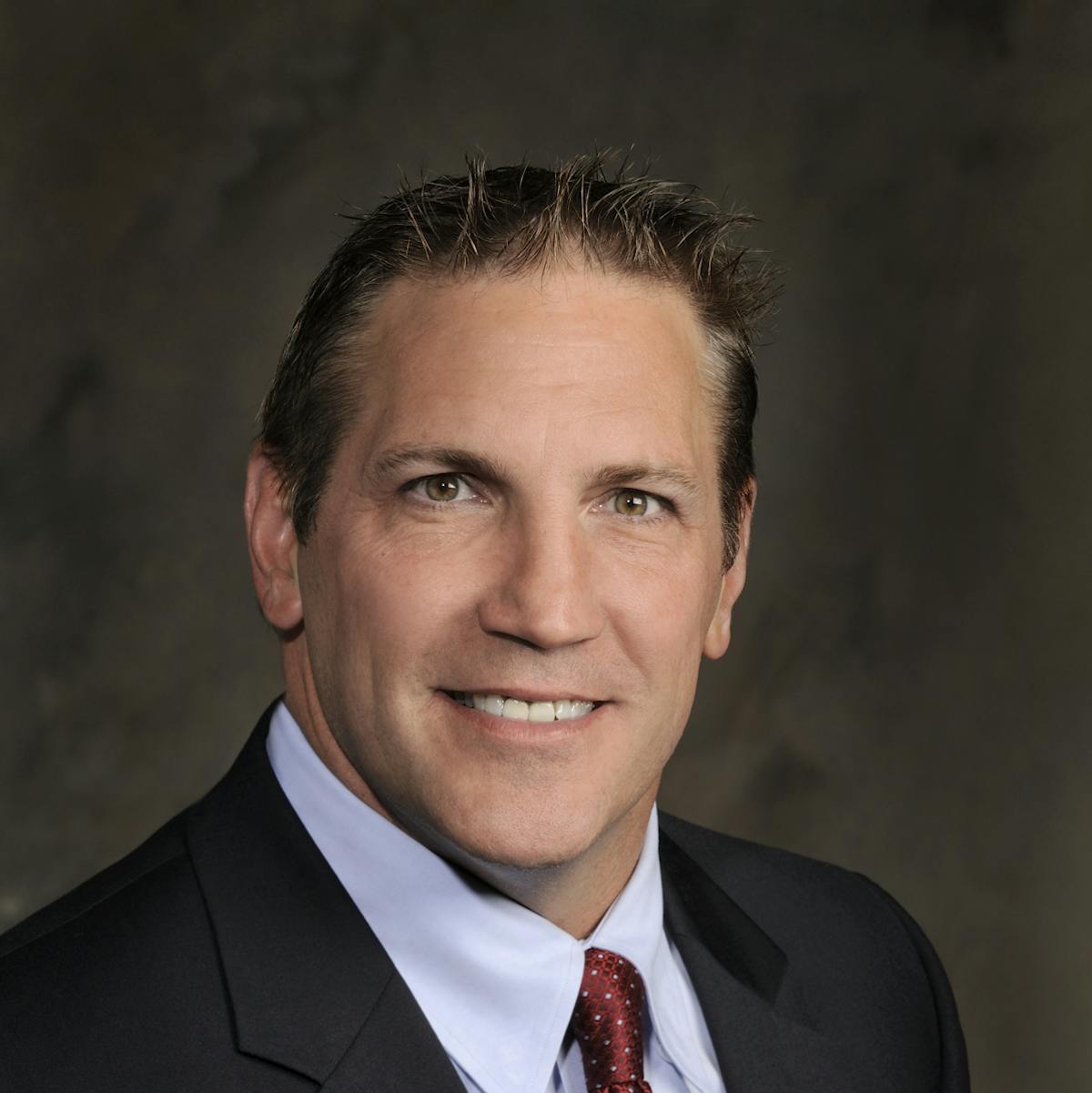 a man wearing a suit and tie smiling and looking at the camera