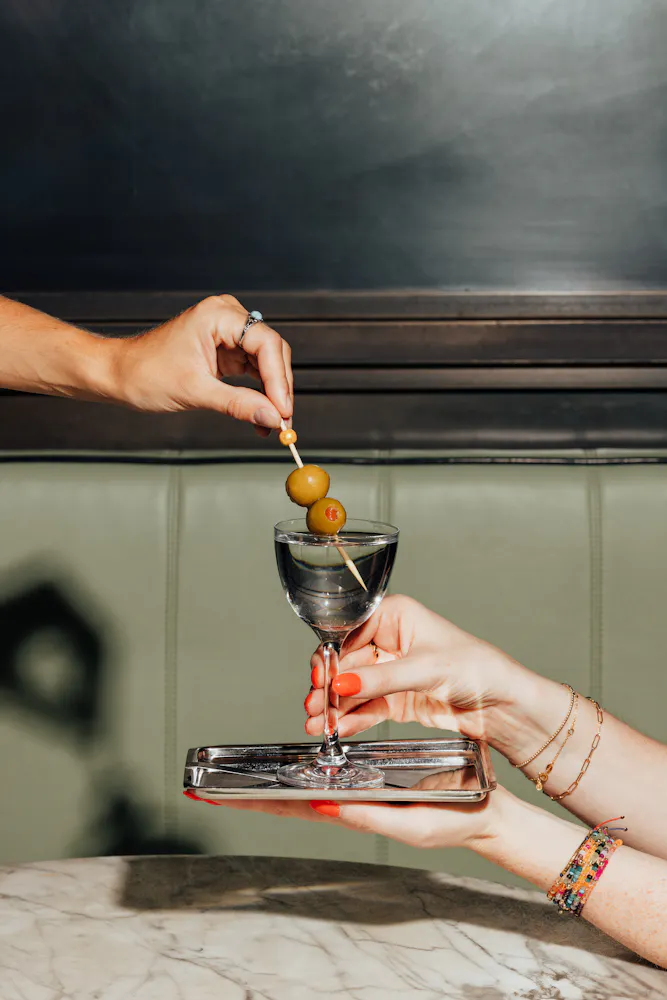 a person holding a glass with a drink and olives