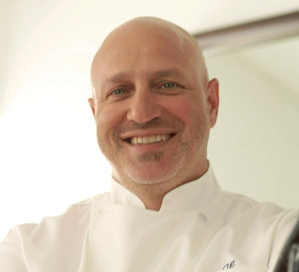 Tom Colicchio wearing a white shirt and smiling at the camera