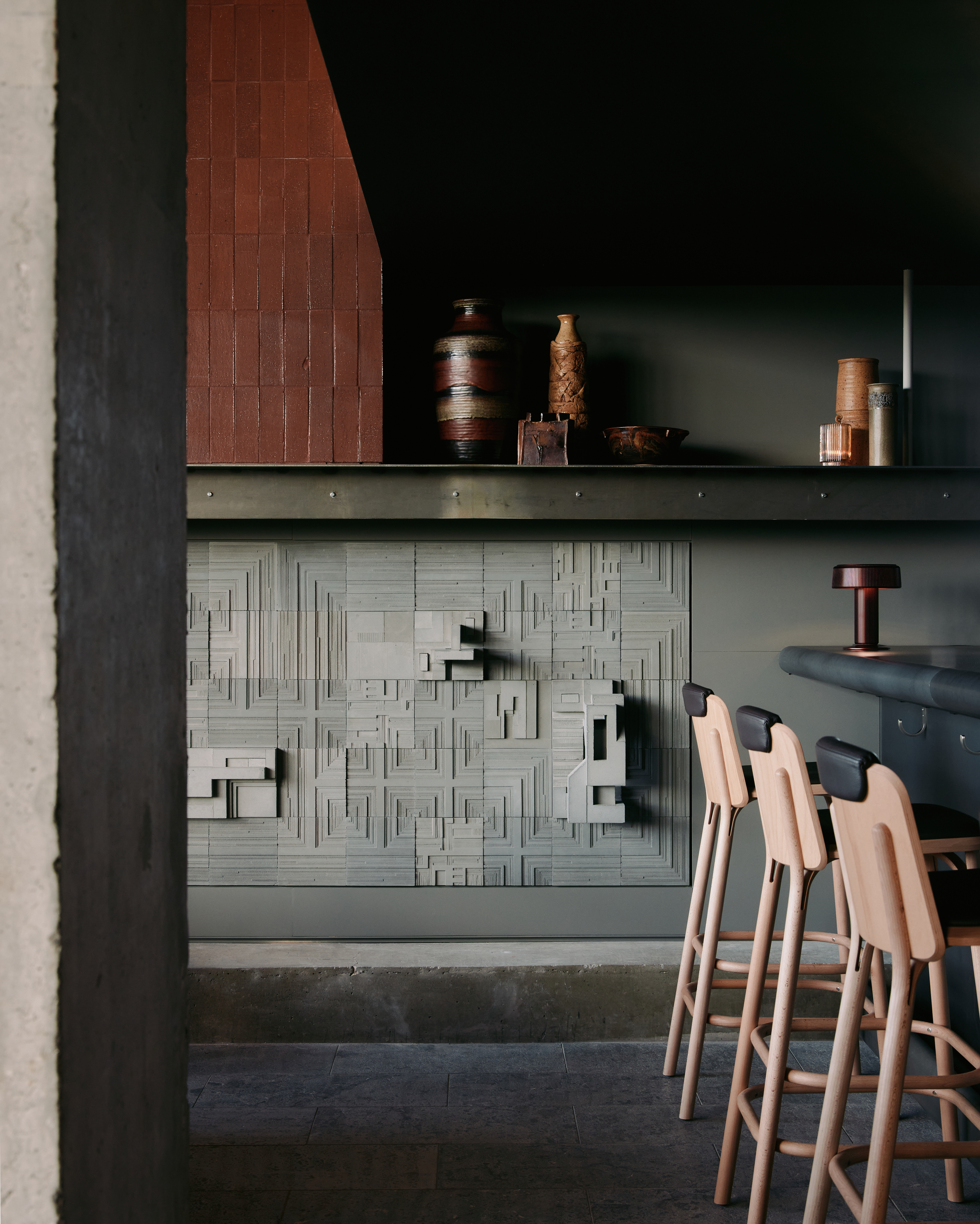 a bar with chairs and a sculpture wall relief in the backgroud
