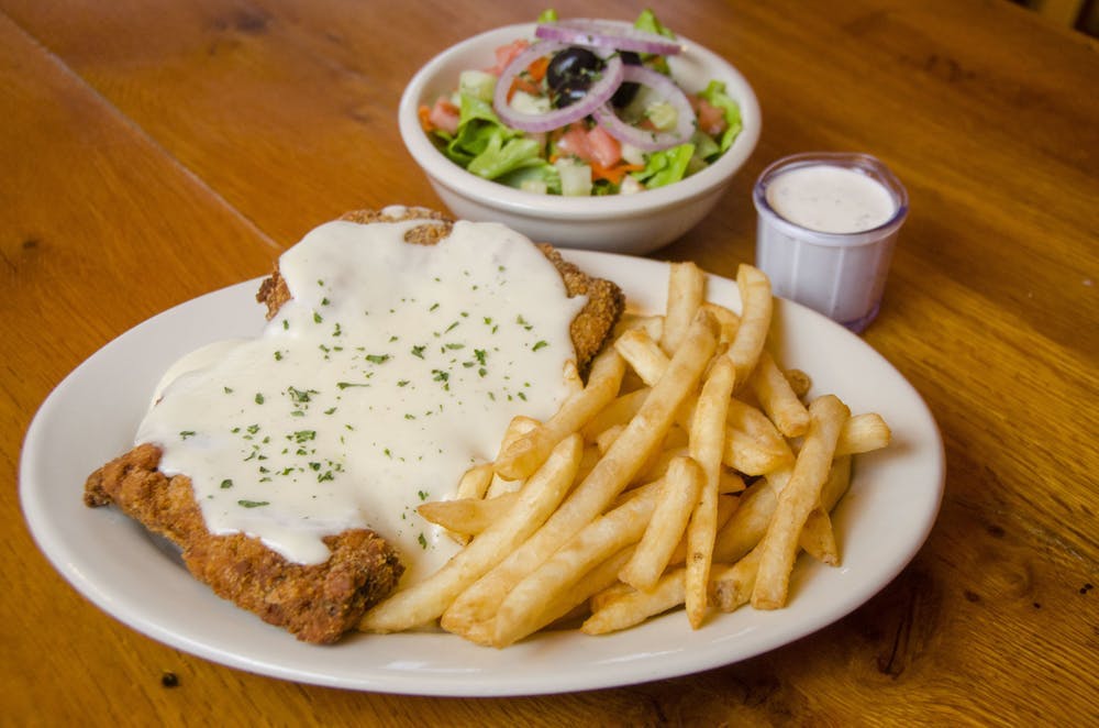 a white plate topped with a grilled chicken breast bathed in white sauce and sided by french fries