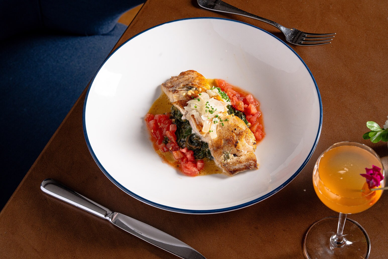 Grilled grouper served over corn pudding and tomato crudo beside a cocktail.