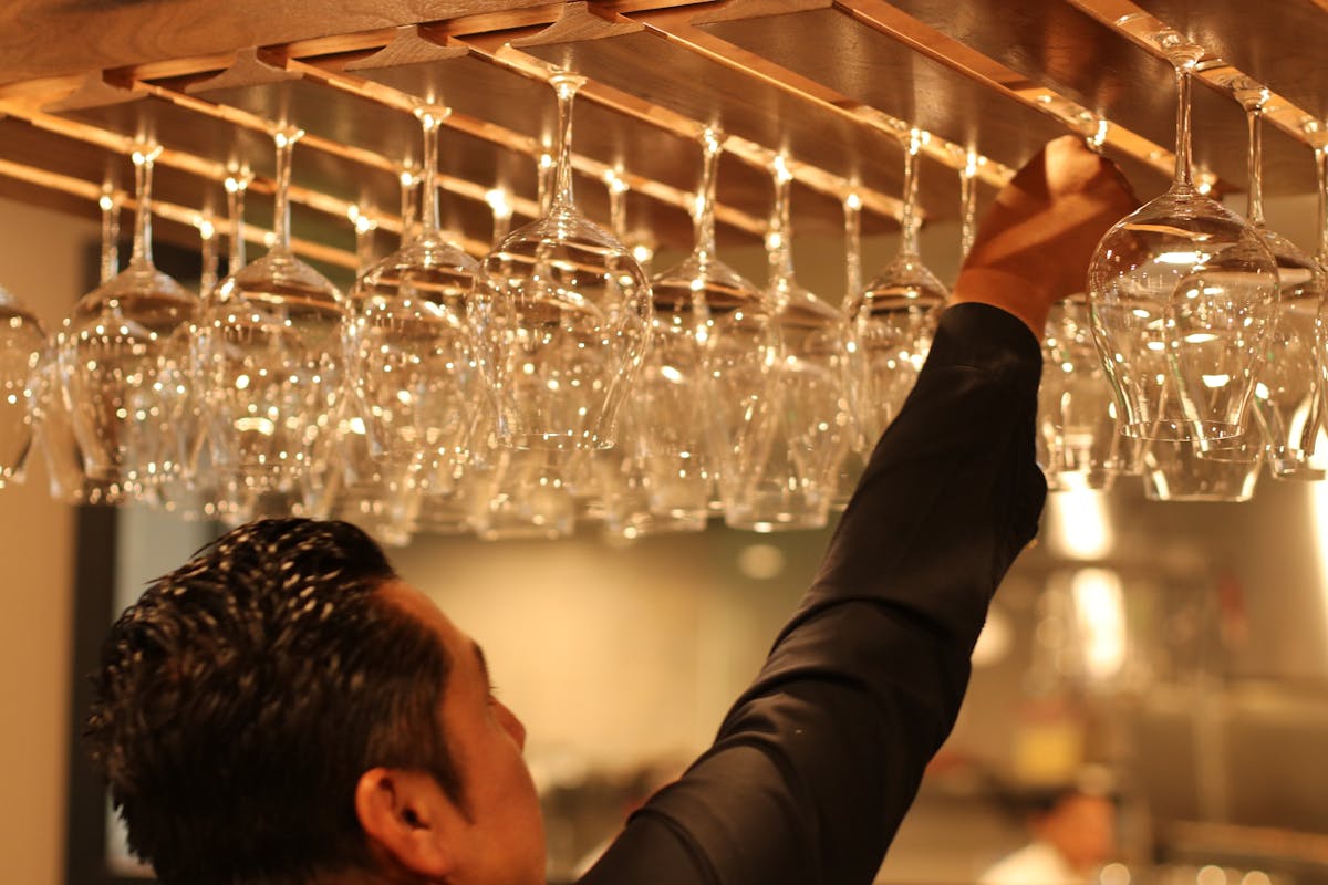 man placing wine glasses in a glass dispenser 